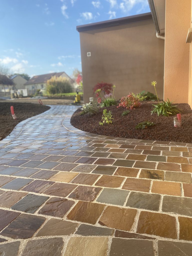 Allée pavée en pierres naturelles et massifs paysagers réalisés par un créateur de jardin dans l’Orne.